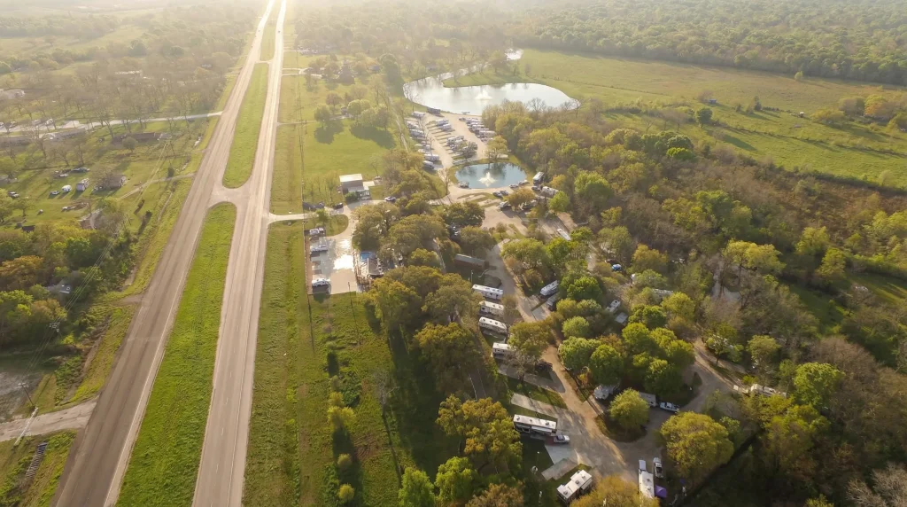 Aerial view of Stonebridge RV Park in Sweeny, Texas, showing RV sites among trees beside a highway, with ponds and parking areas.